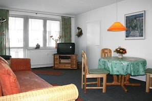 A living room with a sofa, a television on a wooden stand, a dining table with chairs, and a window with curtains. - ||-----------------------at the Amber Spa---------------|| (Zinnowitz)