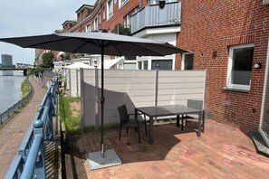 Eine Terrasse im Freien mit Tisch, Stühlen, einem großen Sonnenschirm und Blick auf einen Fluss.