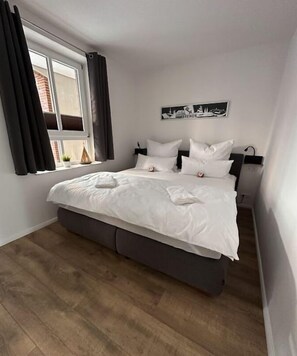 Ein Schlafzimmer mit Bett, Fenster mit Vorhängen, einem Wandbild und einem Nachttisch.