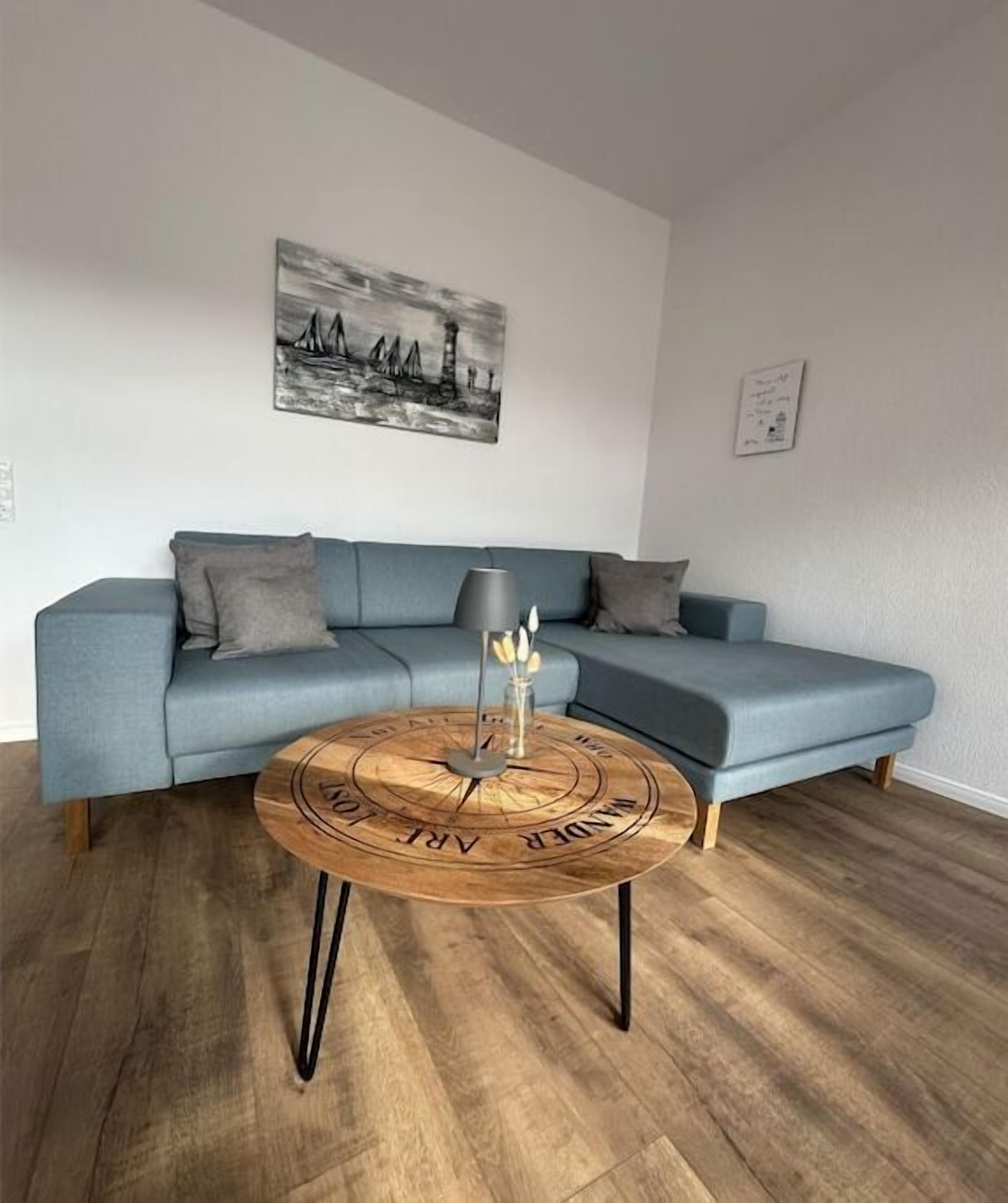 Una sala de estar con un sofá azul, una mesa de centro redonda con tapa de madera y una lámpara negra.