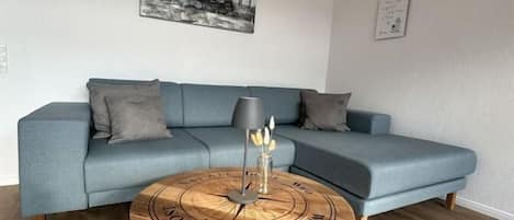 A living room with a blue sofa, a round coffee table with a wooden top, and a black lamp.