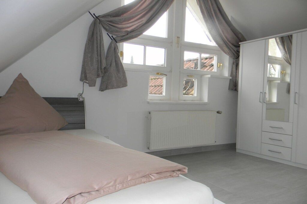 Ein Schlafzimmer mit Bett, Heizkörper, einem Fenster mit Vorhängen und einem Kleiderschrank.