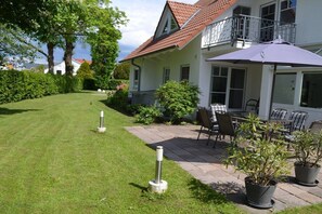 Ein Haus mit einer Terrasse, Sitzgelegenheiten im Freien und einem gepflegten Rasen.