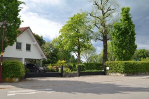 Eine Wohnstraße mit einem weißen Haus, einem schwarzen Auto davor und einem großen Baum.