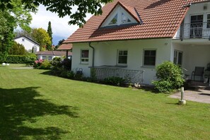 Ein zweistöckiges Haus mit rotem Ziegeldach, einem kleinen Balkon und einem gepflegten Rasen.