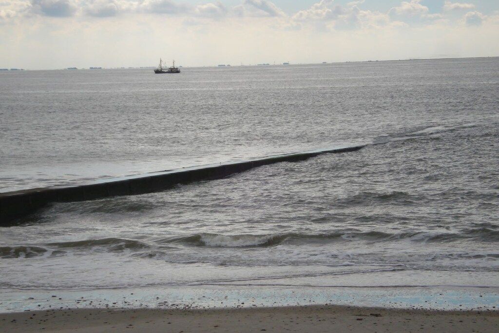 Mar tranquila con un barco a lo lejos y un muro de hormigón en la orilla.