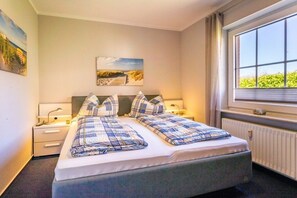 Una habitació d'hotel amb un llit, taules de nit, una finestra amb vistes i obres d'art a les parets.