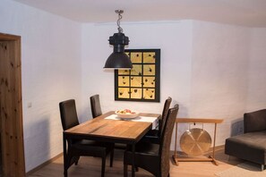 Un coin repas avec une table en bois, des chaises noires, un luminaire suspendu noir et une œuvre d’art accrochée au mur.