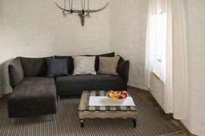 A living room with a dark sofa, a glass coffee table with fruit, and a wall-mounted deer skull. - Holiday apartment with 1 bedroom (0chtendung)