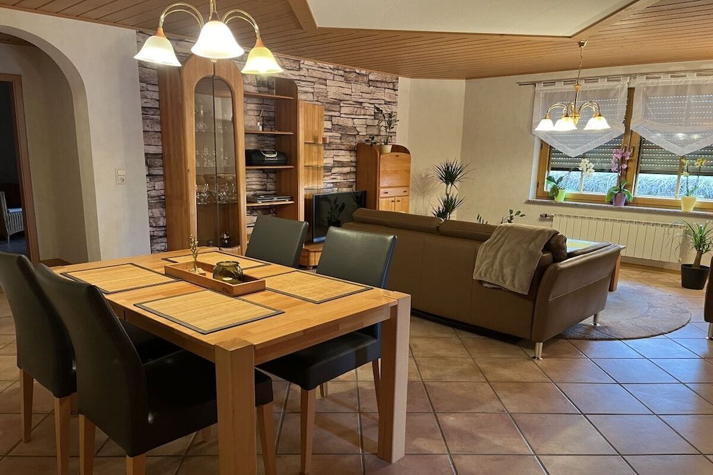 Un coin repas avec une table et des chaises en bois, un canapé marron et un mur en pierre.