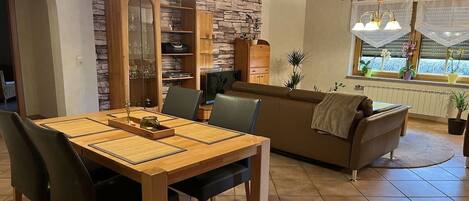 Un coin repas avec une table et des chaises en bois, un canapé marron et un mur en pierre.