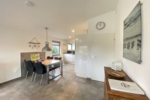 A modern kitchen with a dining area, a clock on the wall, and a painting. - Bungalow with 1 bedroom (Callantsoog)