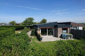 A modern house with a patio, a covered outdoor seating area, and a well-maintained garden. - Bungalow with 1 bedroom (Callantsoog)