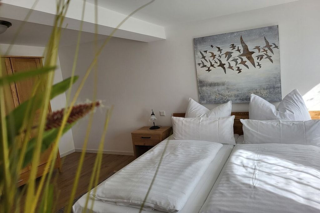 A bedroom with a bed, pillows, a nightstand, a lamp, and a painting on the wall.