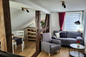 A loft-style room with a wooden staircase, a grey sofa, a small table with a vase, and a white chair. - Holiday apartment with 1 bedroom (Nossentiner Hütte)