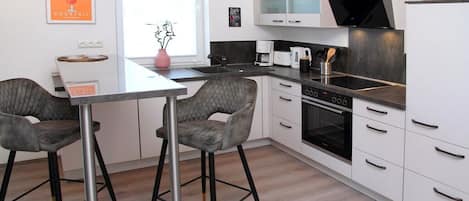 A modern kitchen with a central island, two bar stools, a microwave, a stove, and a sink.