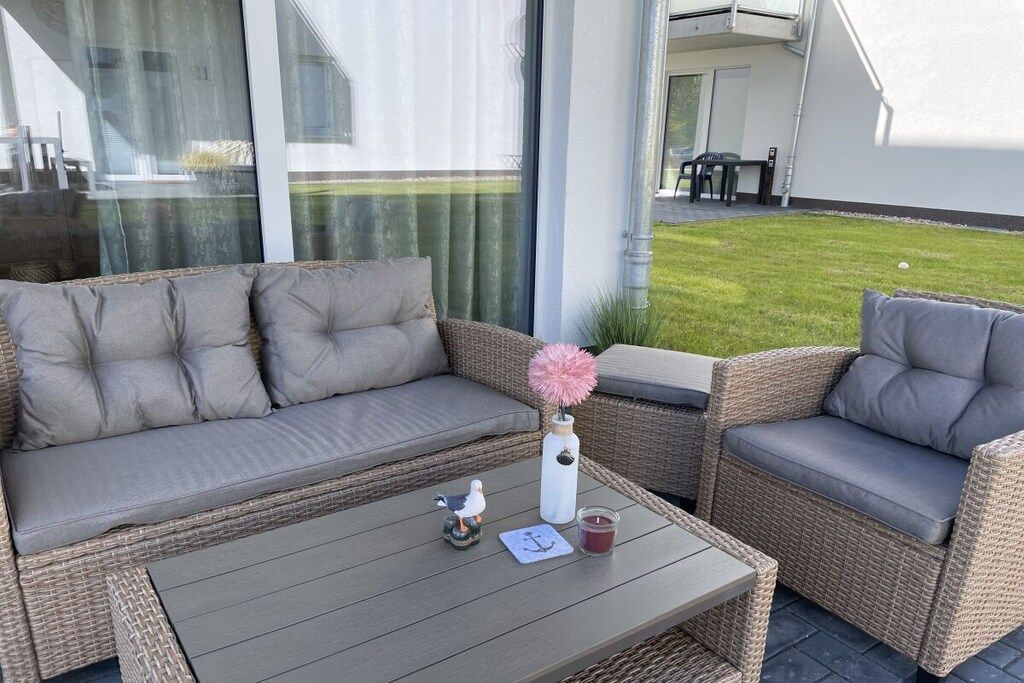 Un ensemble de canapés et de fauteuils en osier est installé sur une terrasse, avec une petite table, une bougie et un objet décoratif.