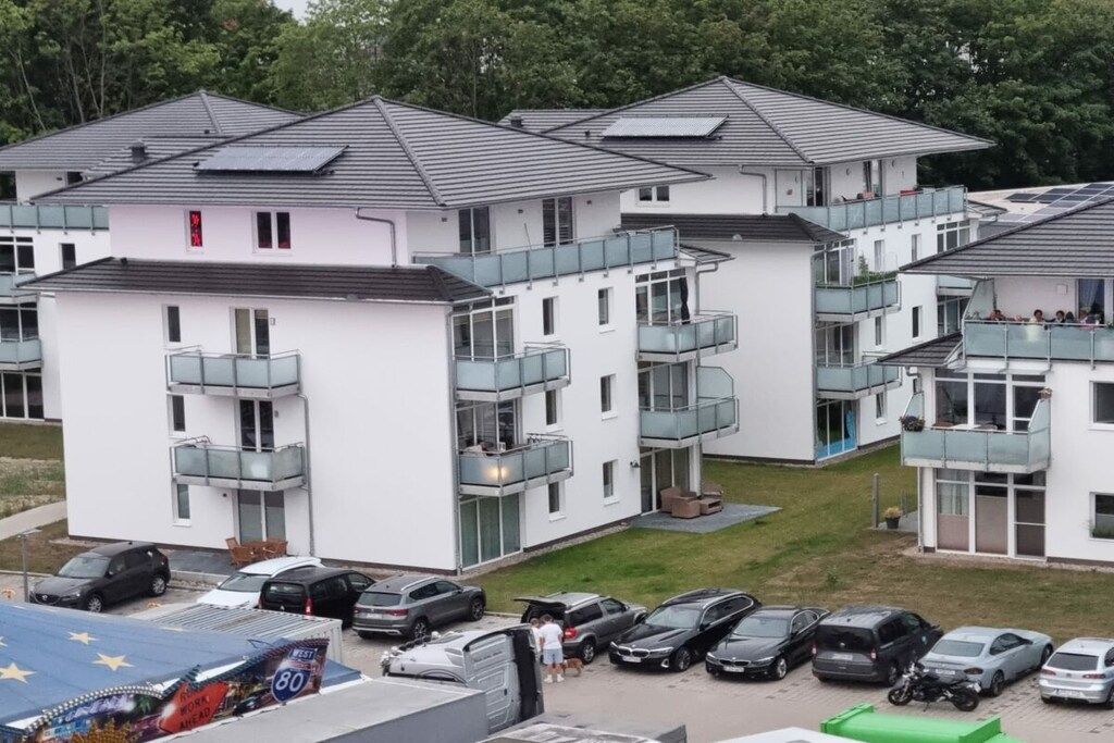 A residential building with multiple balconies, a parking area, and a solar panel on the roof.