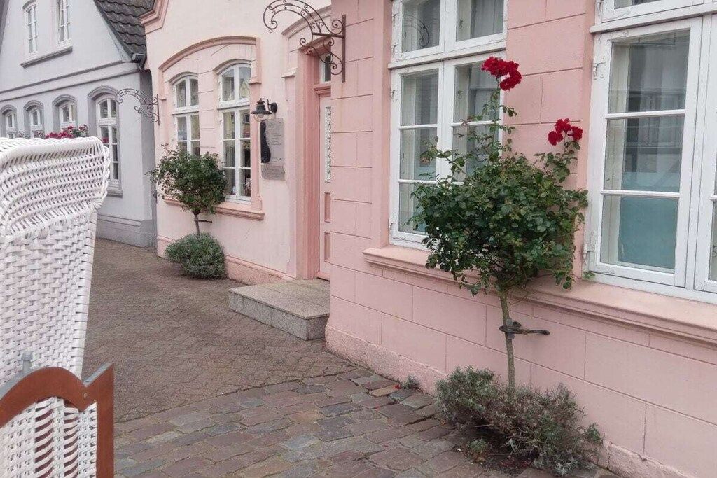 A pink building with a small garden, a white wicker chair, and a red flower.