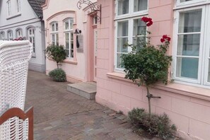 A pink building with a small garden, a white wicker chair, and a red flower. - Holiday apartment with 1 bedroom (Kappeln-Kopperby)
