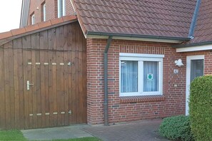 A brick house with a wooden gate, a window with a curtain, and a small bush in the front yard. - Holiday apartment with 1 bedroom (Kappeln-Kopperby)