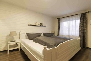 A bedroom with a bed, bedside table, lamp, and curtains. - Holiday home with 2 bedrooms (Simonsberg)