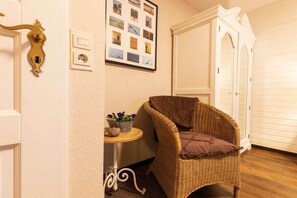 A room with a wicker chair, a small table with a plant, and a wall-mounted photo collage. - Holiday home with 2 bedrooms (Simonsberg)