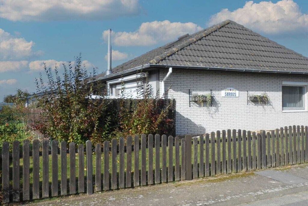 Une maison de plain-pied avec un toit en tuiles, une clôture en bois et une enseigne sur laquelle on peut lire « SIRIUS ».