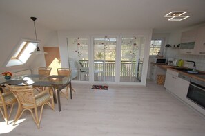 Une cuisine moderne avec des meubles blancs, un coin repas avec des chaises en osier et une grande porte-fenêtre coulissante donnant sur un balcon.