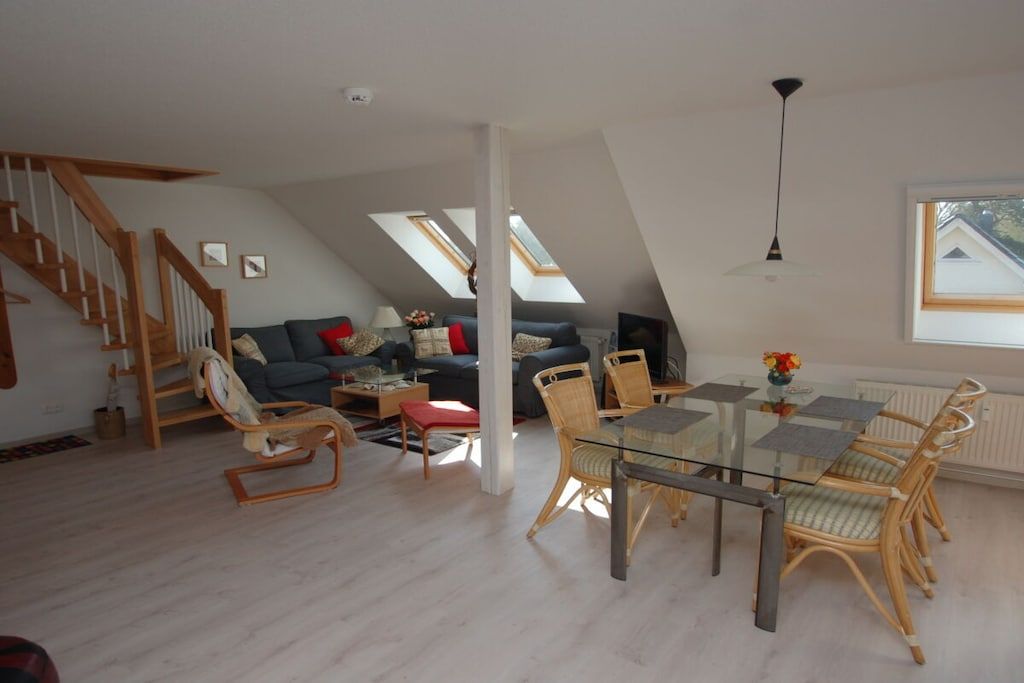Un loft espacioso con comedor, escalera y sala de estar con sofá y sillones.