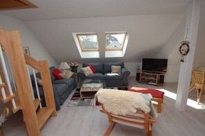 A modern living room with a sofa set, a glass coffee table, a television, and a wooden chair. - Holiday apartment with 1 bedroom (Ostseebad Prerow)