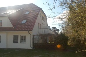 Une maison à deux étages, avec un toit recouvert de tuiles rouges, un balcon et un petit jardin.