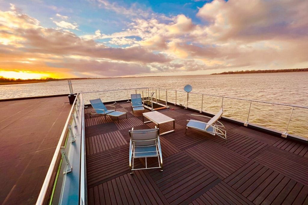 A deck with lounge chairs and tables, overlooking a body of water.