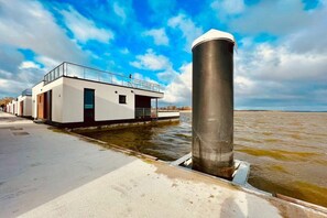 A modern building with a flat roof and a cylindrical structure adjacent to a body of water. - Holiday home with 2 bedrooms (Ribnitz-Damgarten)