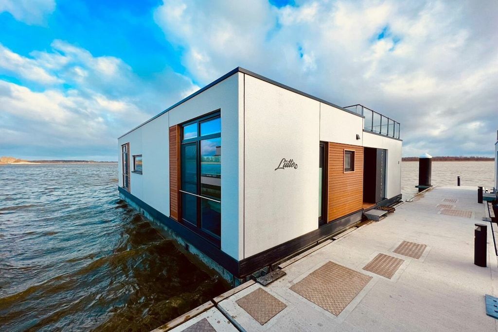 Un hotel moderno flotante con fachada de vidrio, detalles de madera y una placa con el nombre en el costado.