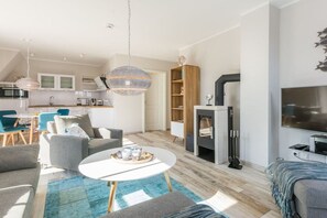 A modern living room with a fireplace, a dining area, and a kitchen in the background. - Holiday apartment with 1 bedroom (Zingst)