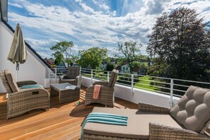Een balkon met rieten meubels, een tafel en uitzicht op een groen landschap.