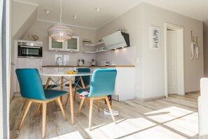 Een moderne keuken met witte kasten, een inbouwoven en een eethoek met turquoise stoelen en een witte tafel.