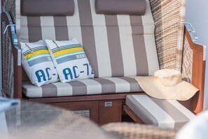 Un fauteuil de relaxation à rayures avec des coussins, un chapeau de paille et une chaise en osier.