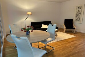 Ein modernes Wohnzimmer mit einem runden Tisch, weißen Stühlen, einem schwarzen Sofa, einer Stehlampe und einem gerahmten Kunstwerk an der Wand.