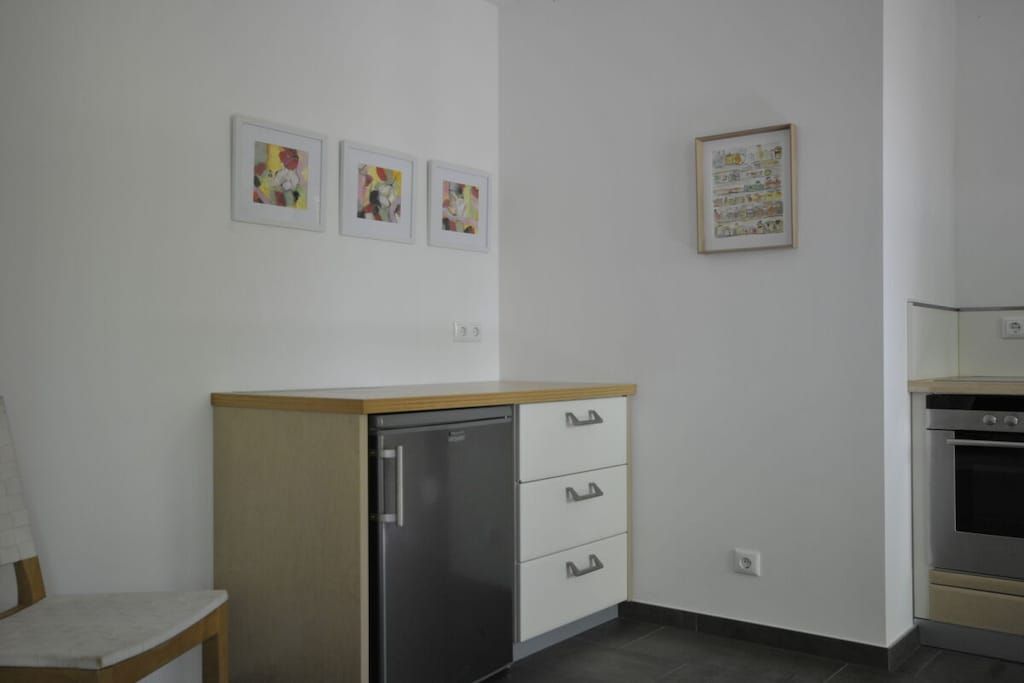 A kitchen with a refrigerator, oven, and a dining area with a chair.