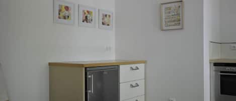 A kitchen with a refrigerator, oven, and a dining area with a chair.