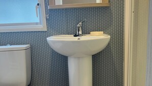 Une salle de bain avec un lavabo sur colonne blanc, des toilettes et un espace douche.
