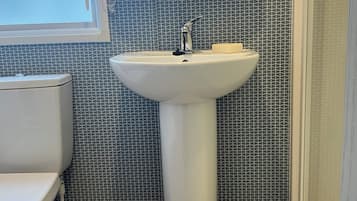 Un baño con lavamanos pedestal blanco, inodoro y cabina de ducha.
