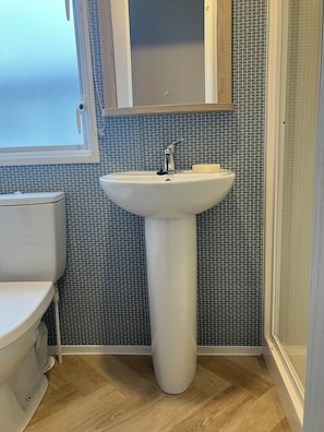 Un baño con lavamanos pedestal blanco, inodoro y cabina de ducha.