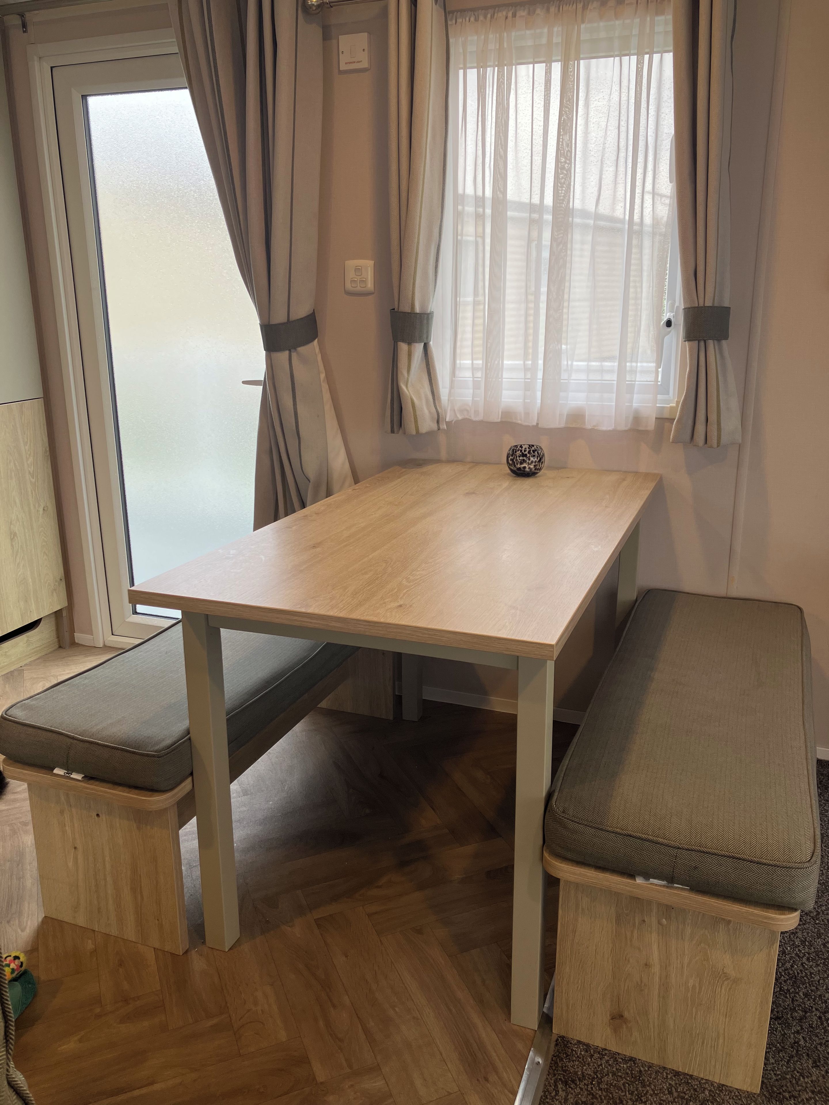 Una habitación pequeña con una mesa de madera, dos bancos y una ventana con cortinas.