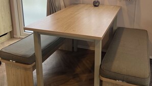 Une petite pièce avec une table en bois, deux bancs et une fenêtre avec des rideaux.