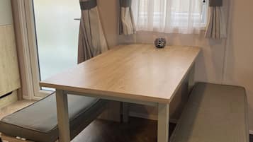 Una habitación pequeña con una mesa de madera, dos bancos y una ventana con cortinas.