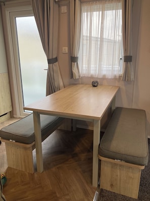 Una habitación pequeña con una mesa de madera, dos bancos y una ventana con cortinas.