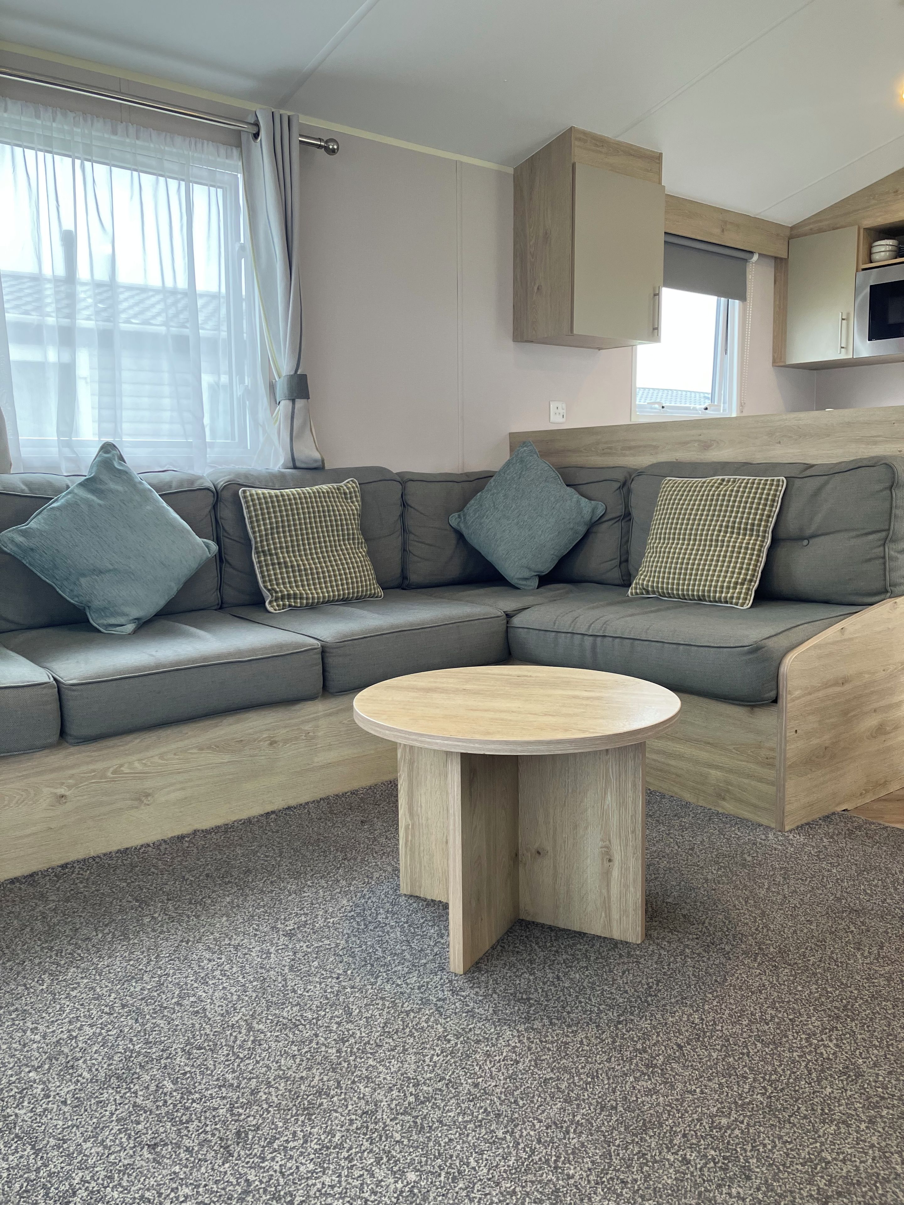 A modern RV interior with a sectional sofa, a round wooden table, and a kitchenette area.